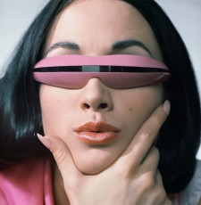 Model wearing pink plastic sunglasses with a single band of lens by John Rawlings (1965)